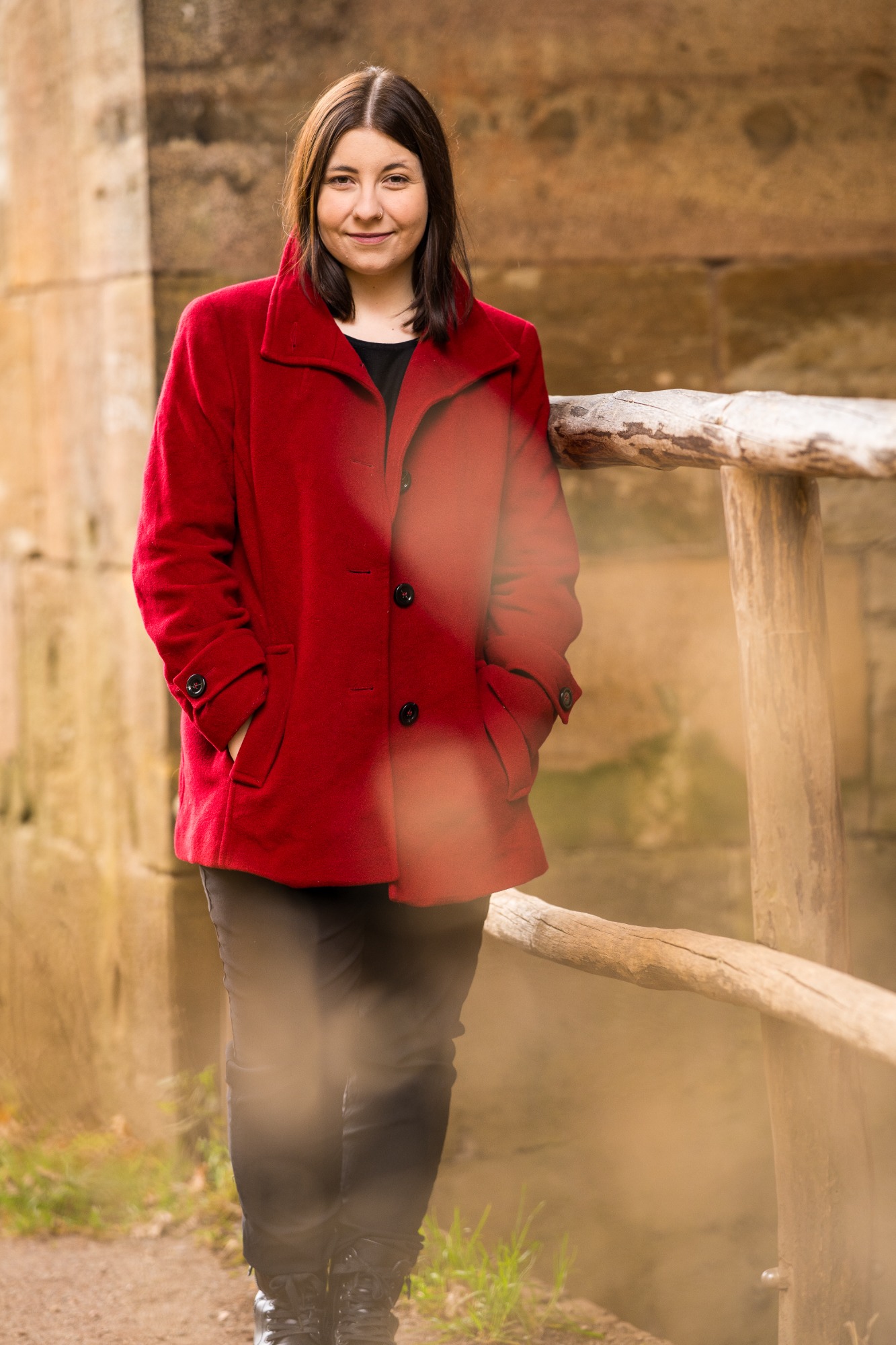 Portait Frau in einem roten Mantel steht lächelnd neben einem Holzgeländer.